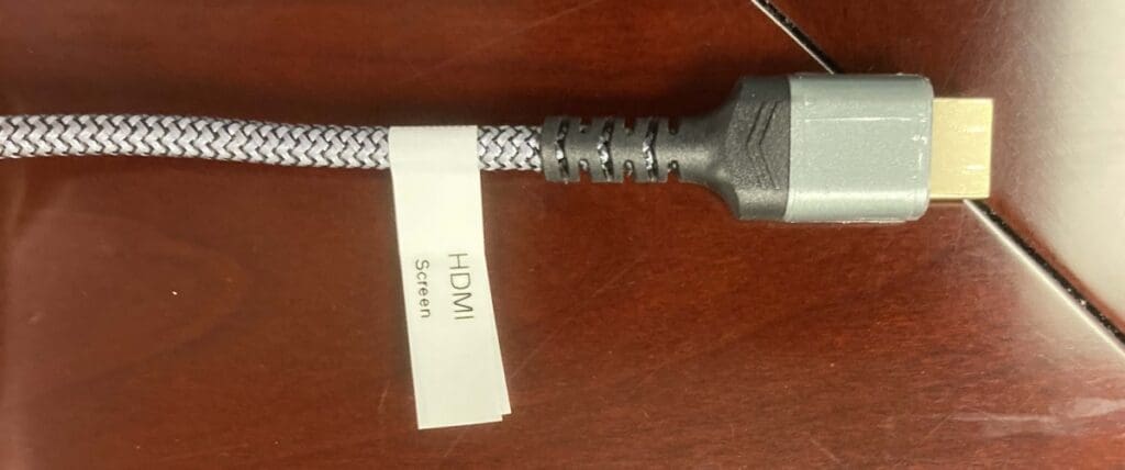 HDMI cable with a white label reading "HMDI" and "Screen" in black, sitting on a wooden table.