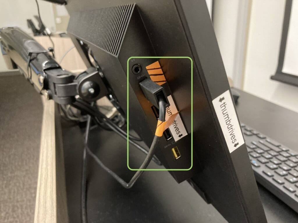 side of a computer monitor showing a usb cable plugged in with an orange flagged wrapped around it.
