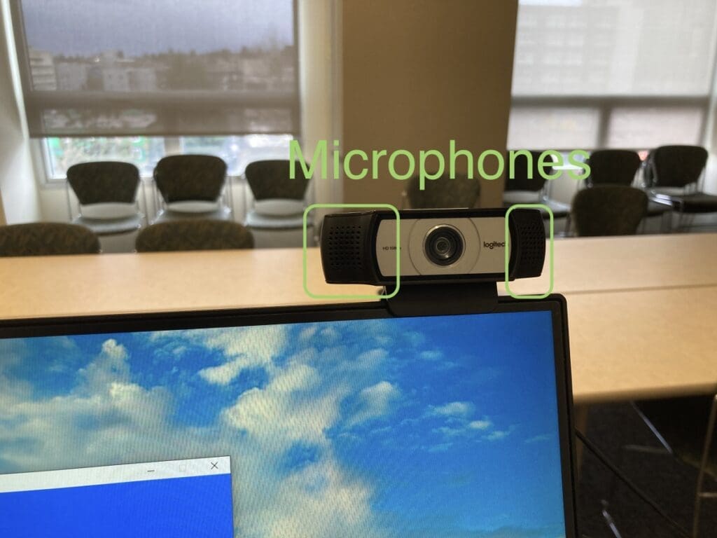 Camera attached to the top of a computer monitor with the word Microphones written in green above it.