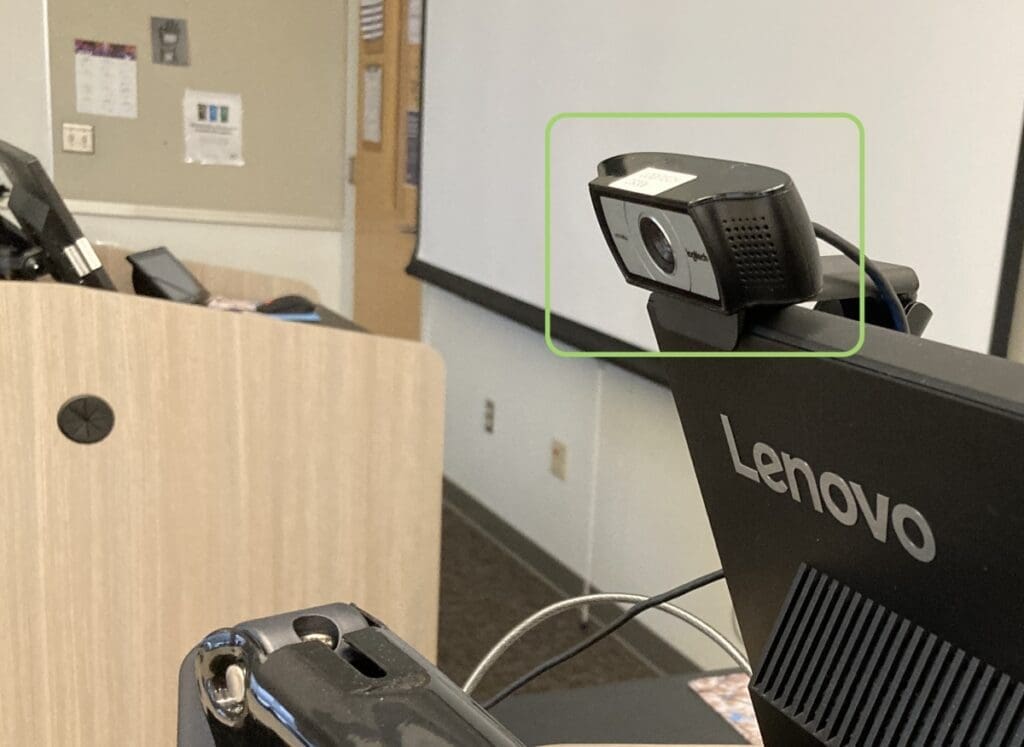 Camera attached to the top of a computer monitor, facing outward toward a classroom.