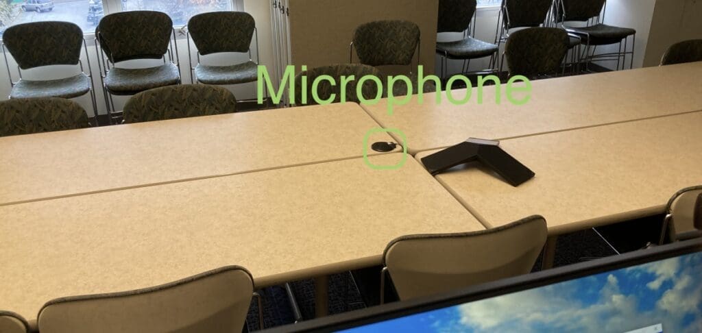 Small microphone sitting on top of a wooden table circled in green with the word Microphone printed above it also in green