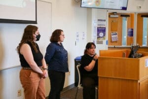 Student presenters speak from the front of the room.