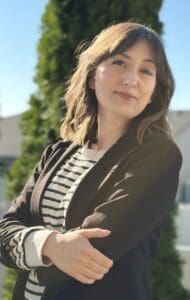 Adely Ruiz folds her arms while posing for the camera. She's wearing a black and white-striped shirt and a charcoal blazer.