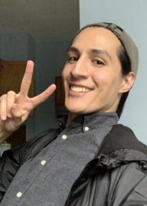 Chris Vera holds up a peace sign while smiling at the camera.