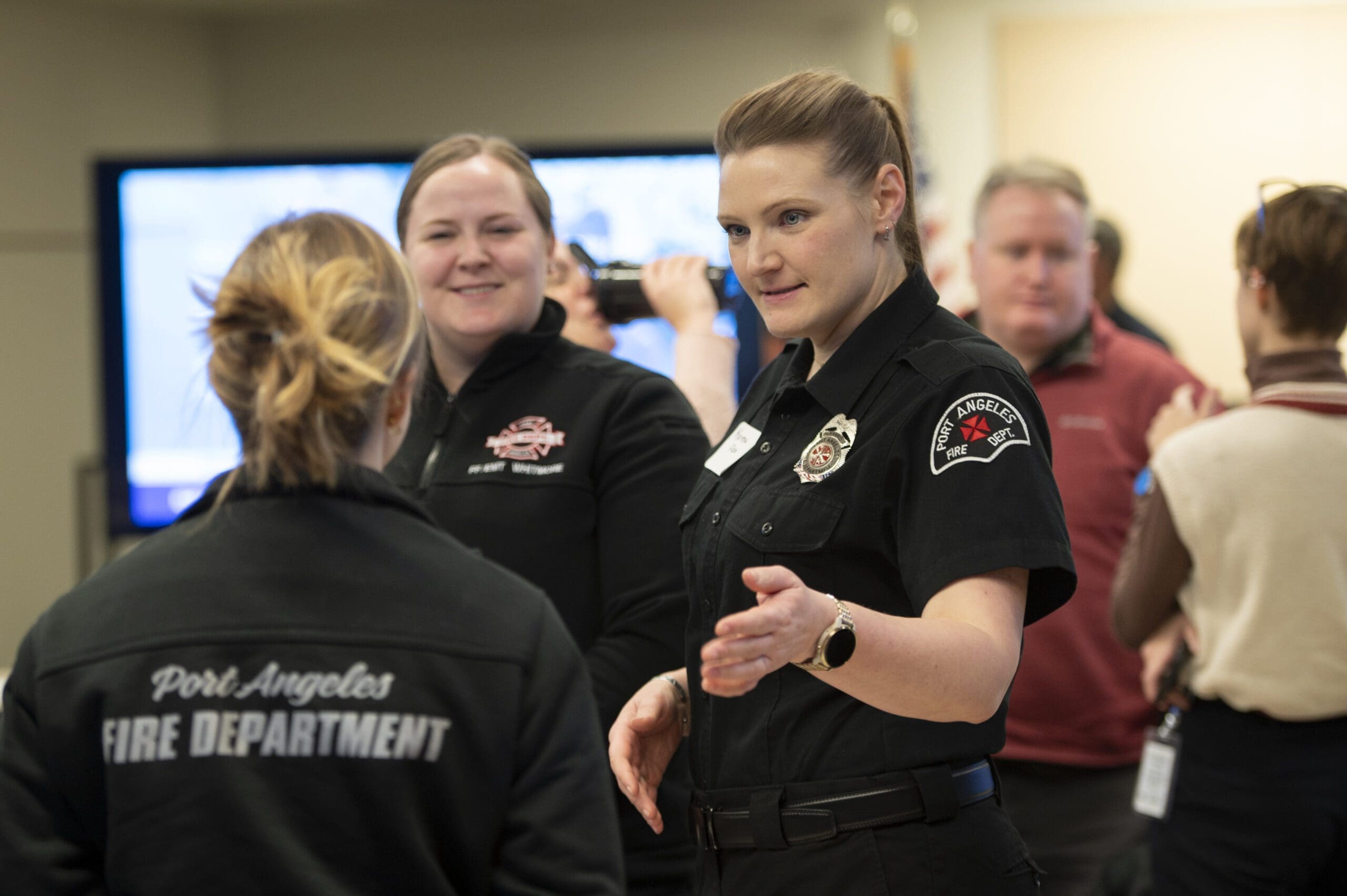 First responders stand and converse indoors during a training session. The woman closest to the camera has Port Angeles Fire Department patch on her uniform.