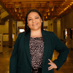 A young dark-haired woman smiles into camera while wearing a blazer and black pants.