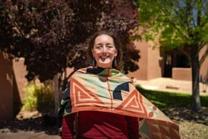 Professor Evans-Campbell smiles on a sunny day, while wearing a multi-colored shawl over a red shirt, and teal and red earrings.