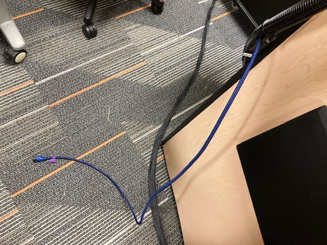long blue cable cascading towards the gray and multicolored carpet and going past a wooden tabletop