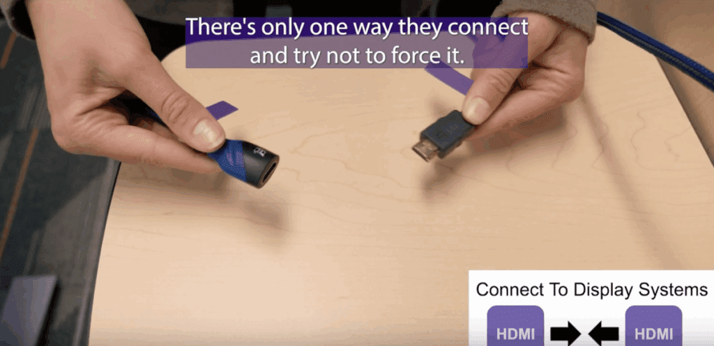 Two HDMI cables being held next to one another by two different white skin-tone hands.