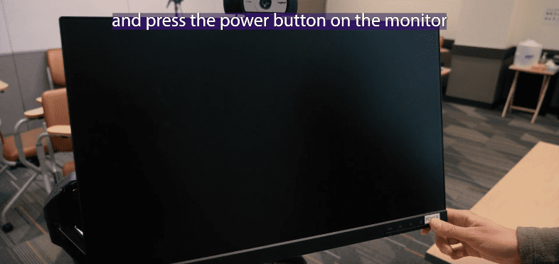 Desktop monitor with a hand reaching towards it to press the on button.