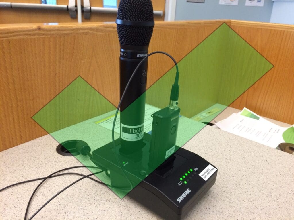 Black microphone in a charger, sitting on a podium with a large green check mark overlaying the entire image.