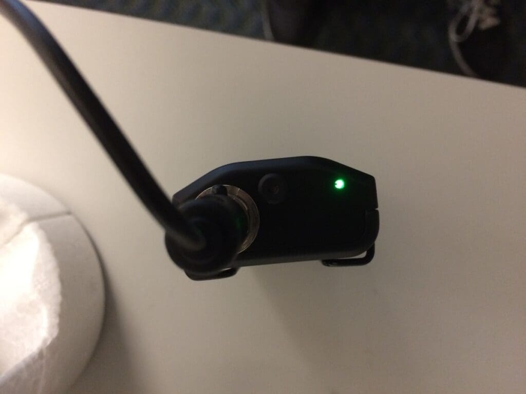 Black microphone connection box, with a green light on at the top, sitting on a podium.