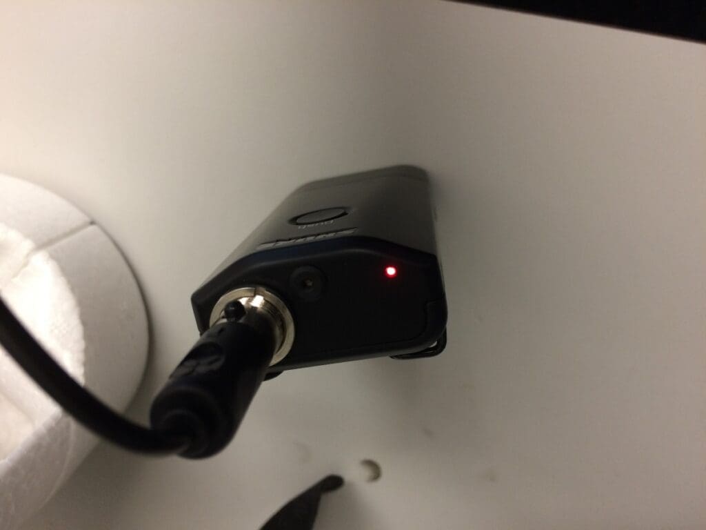 Black microphone connection box, with a red light on at the top, sitting on a podium.